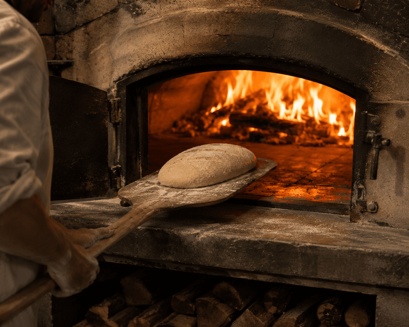 A baker sliding a fresh loaf into a wood-fired stone oven